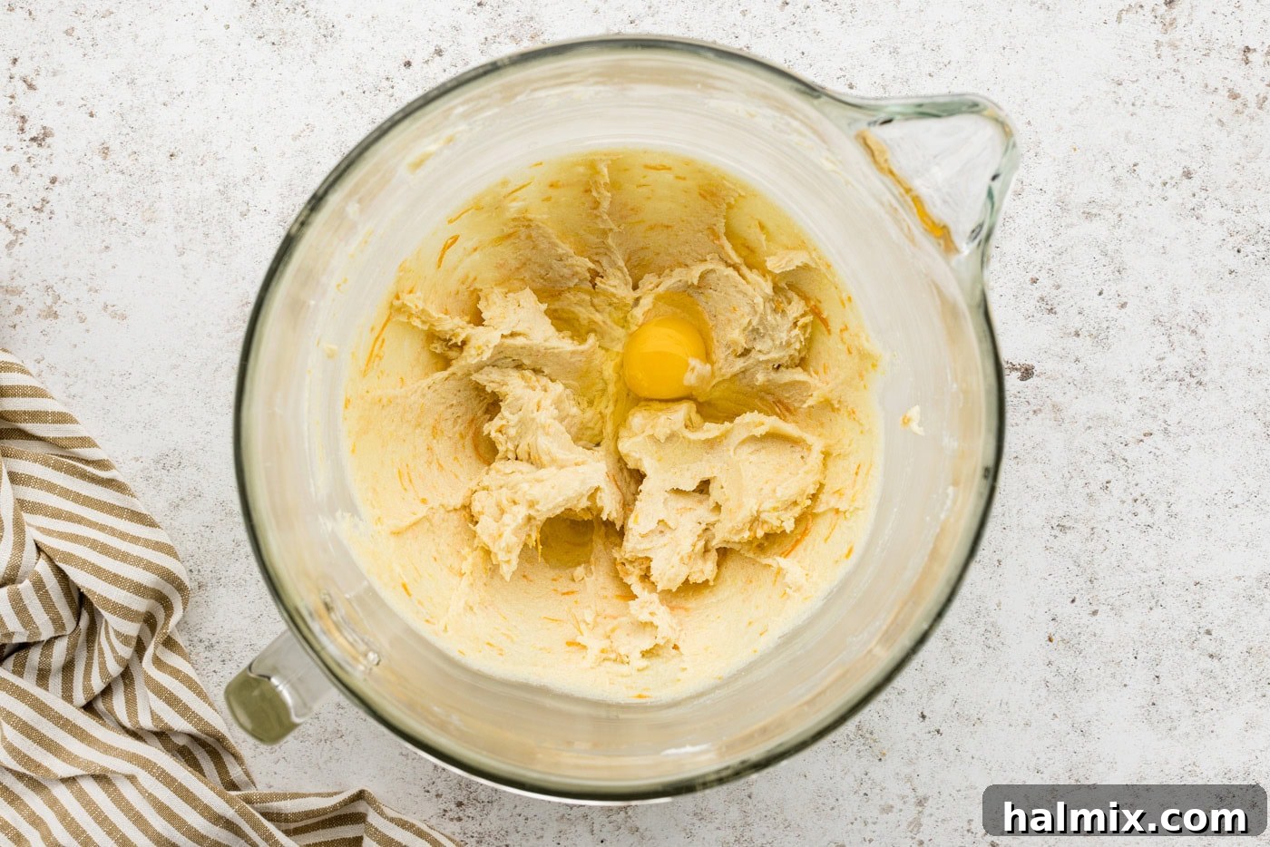 A cracked egg added to the butter and sugar mixture in a stand mixer bowl, ready to be beaten.