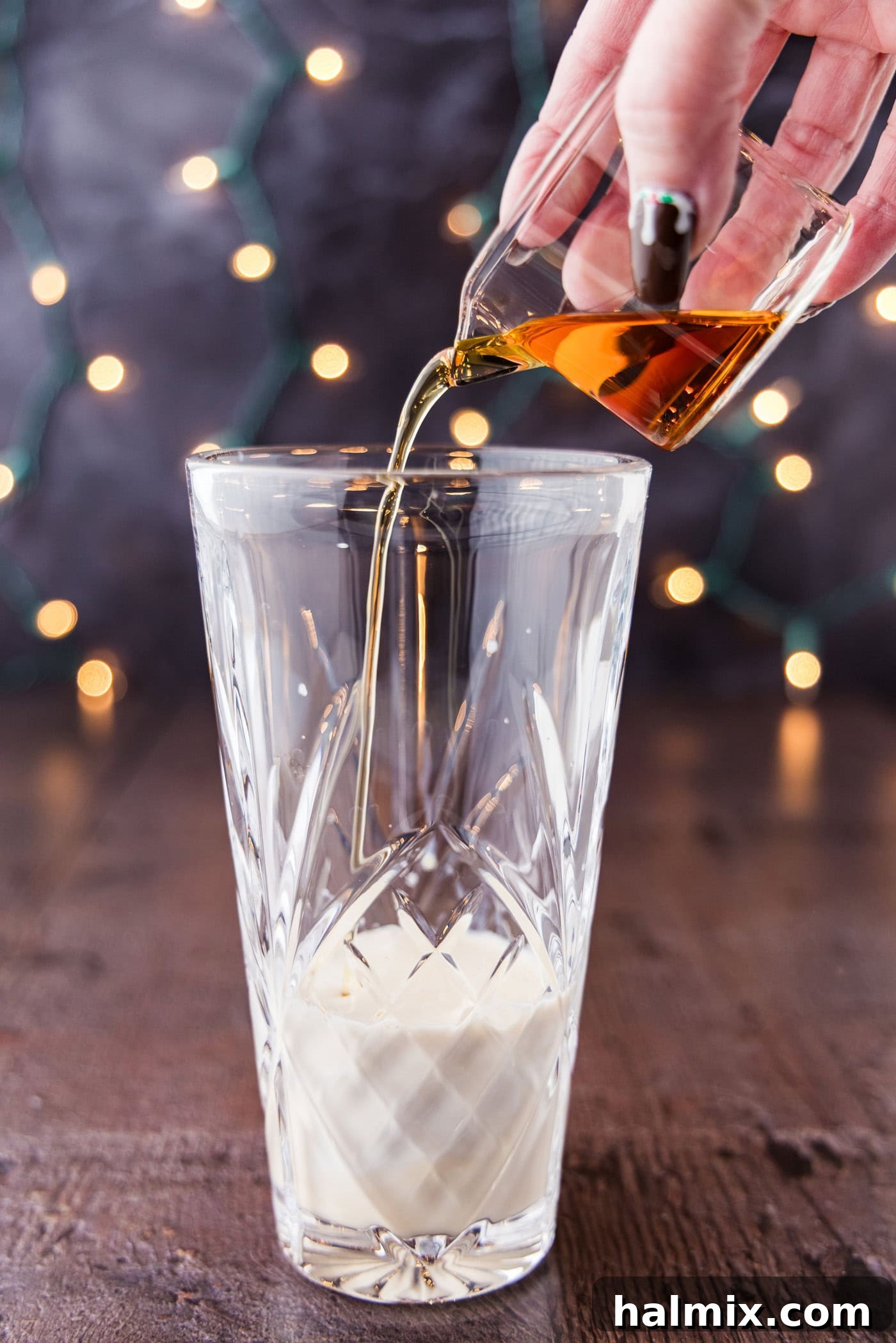 A close-up shot of amaretto being poured into a cocktail shaker glass, which already contains ice and other ingredients, ready for mixing.