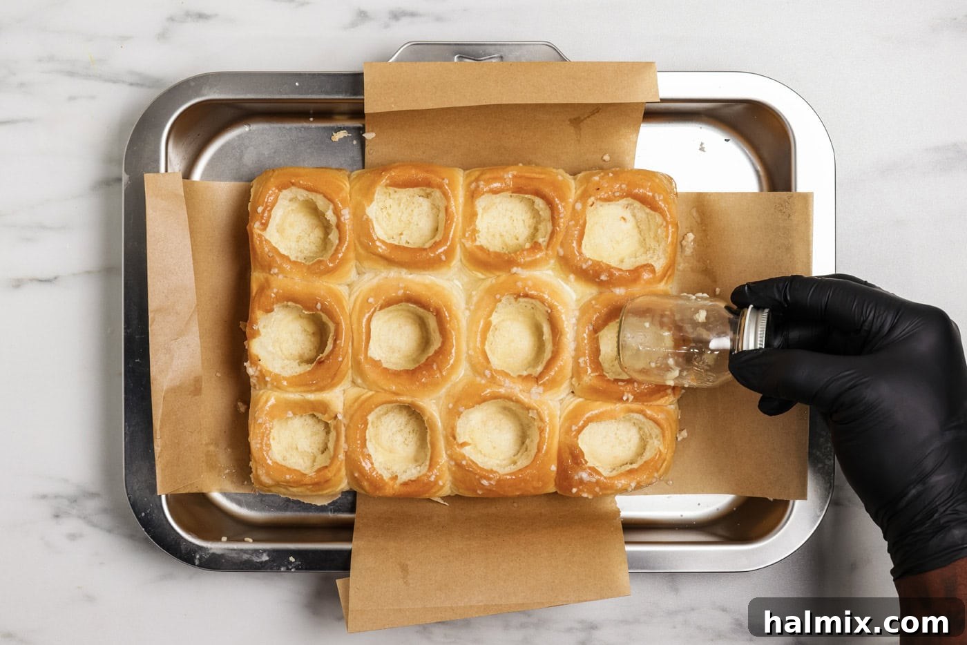 Pocket-Sized Meatball Delights 6 A hand using a mini mason jar to create even, round holes inside soft dinner rolls for the slider filling.