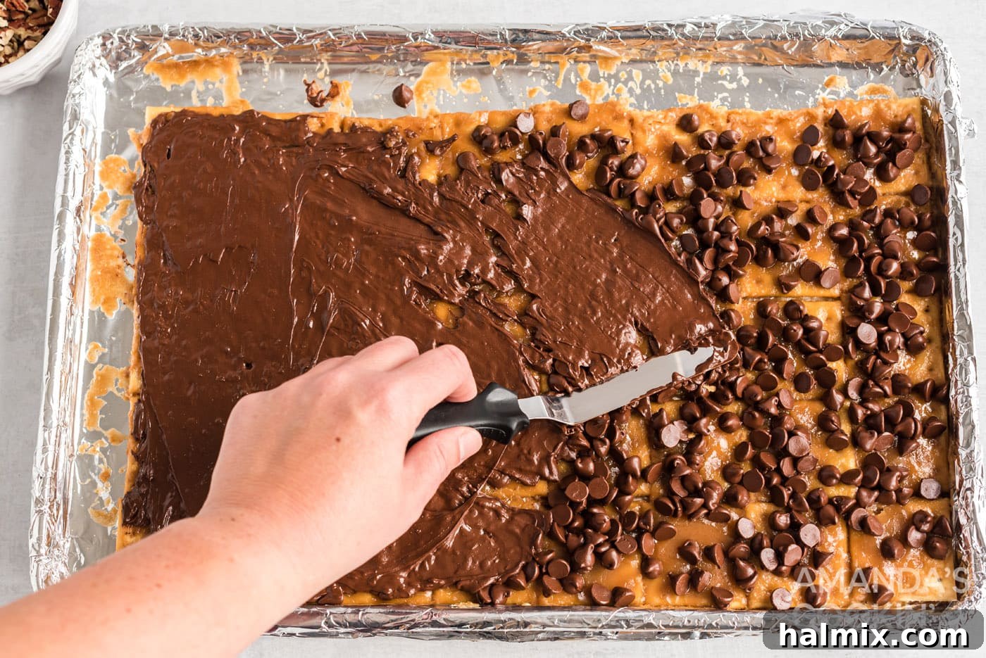 Spatula spreading melted chocolate over the saltine toffee base