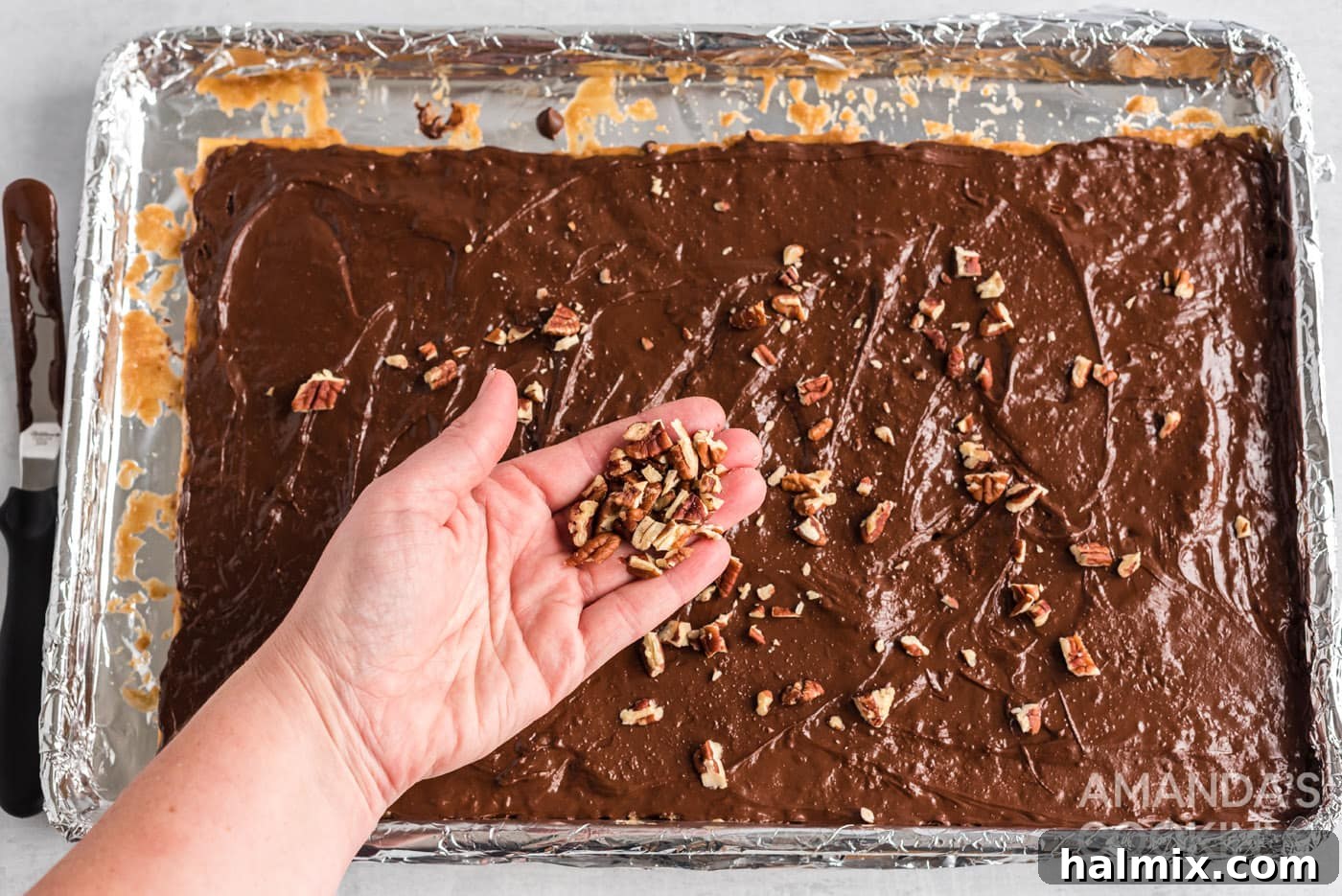 Chopped nuts being sprinkled on top of the melted chocolate layer of saltine toffee