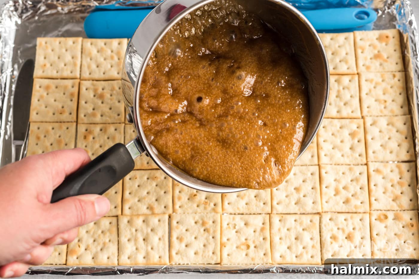 Pouring hot caramel mixture over saltine crackers on a baking sheet