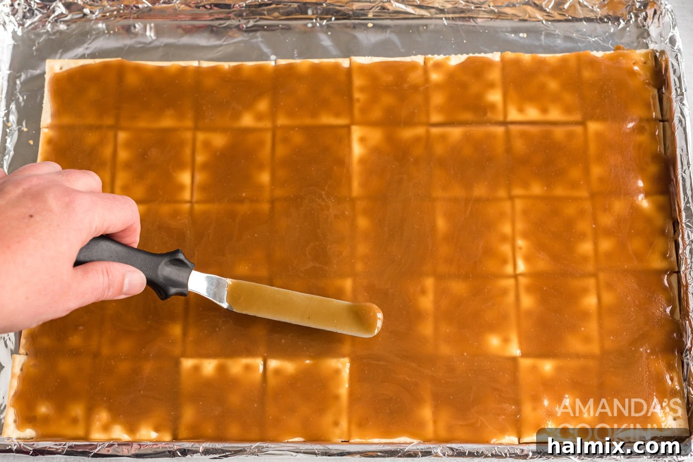 Spatula spreading caramel evenly over the saltine crackers