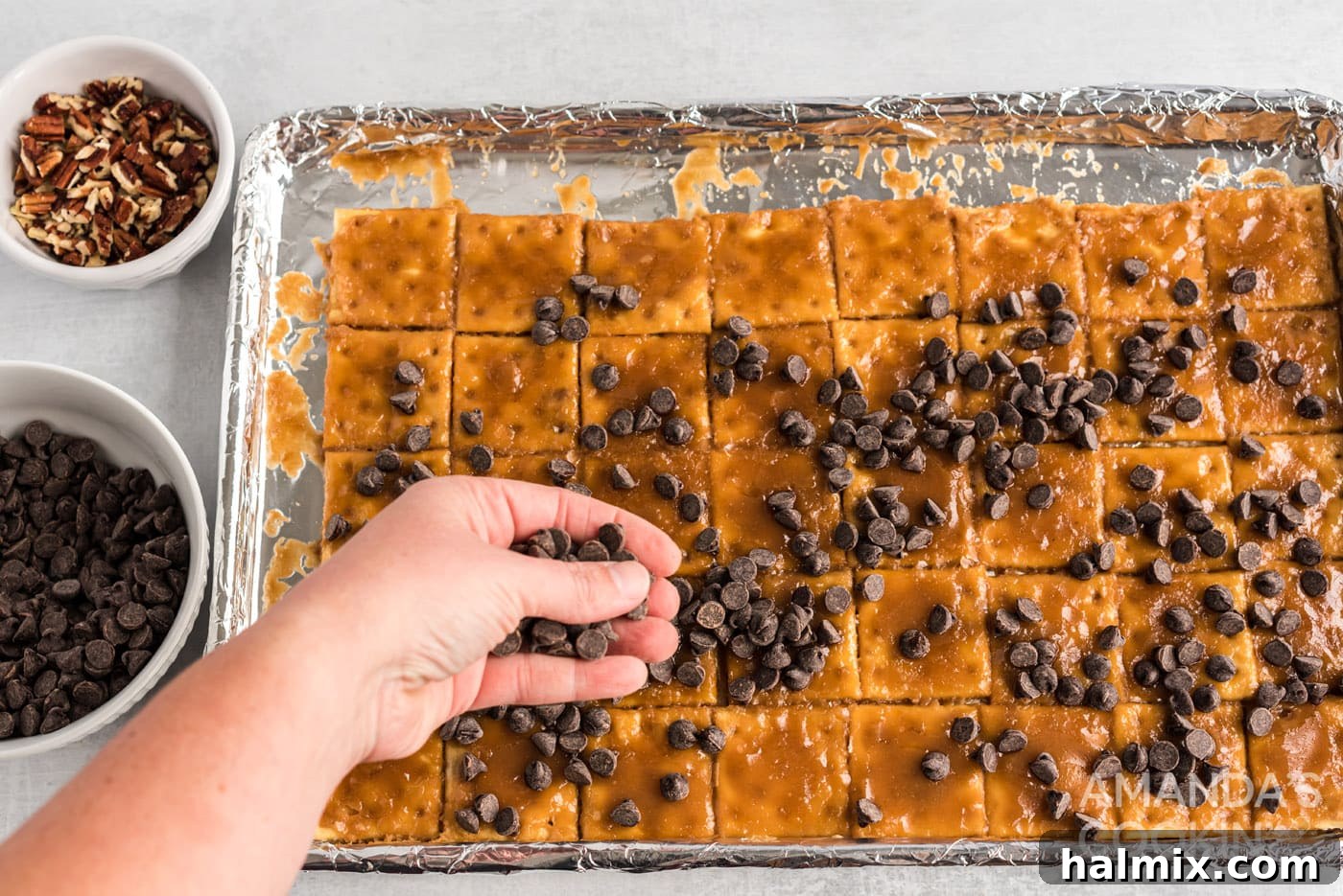 Hand sprinkling chocolate chips onto hot caramel-covered crackers