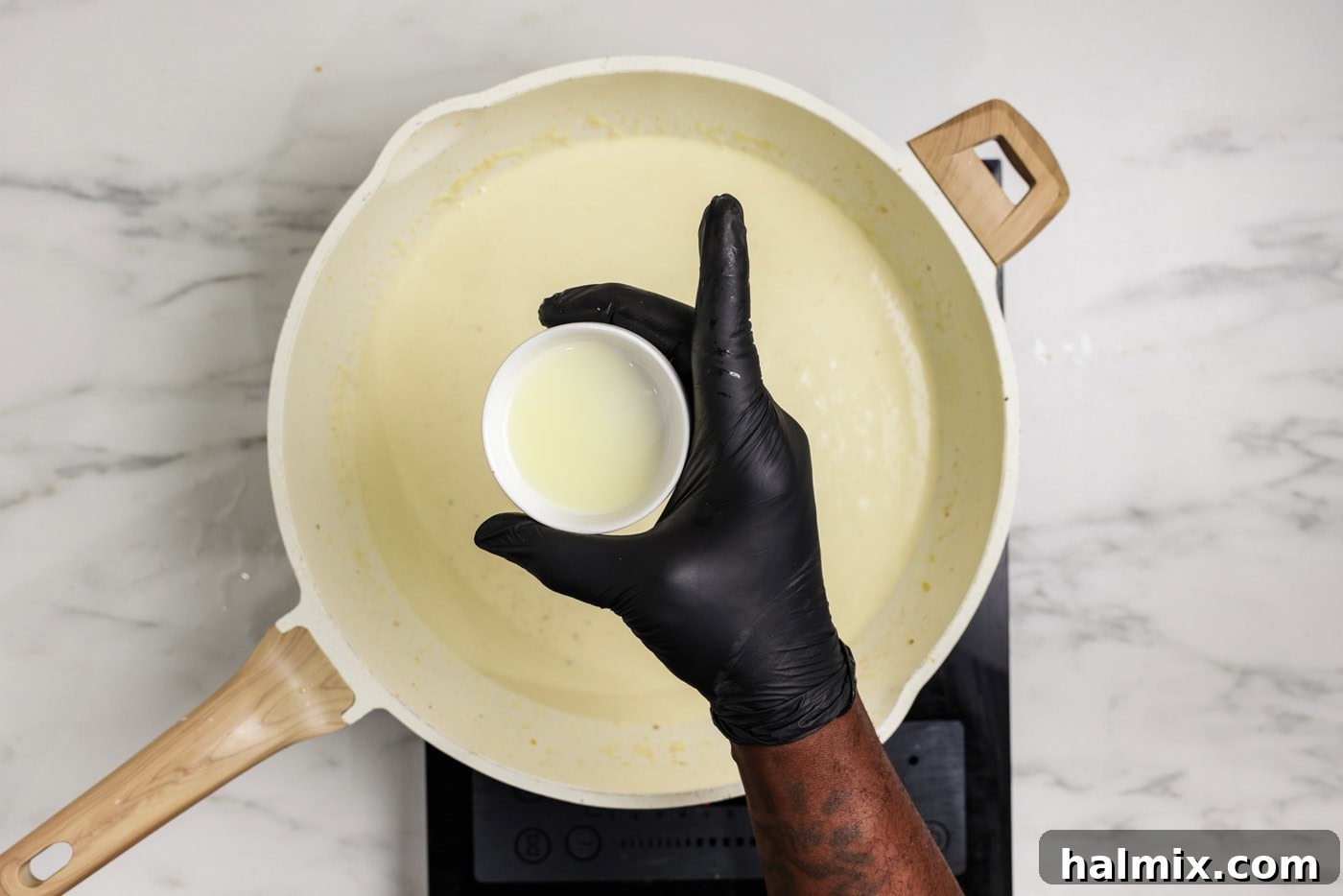 hand holding a small bowl of lemon juice over a skillet of garlic cream sauce