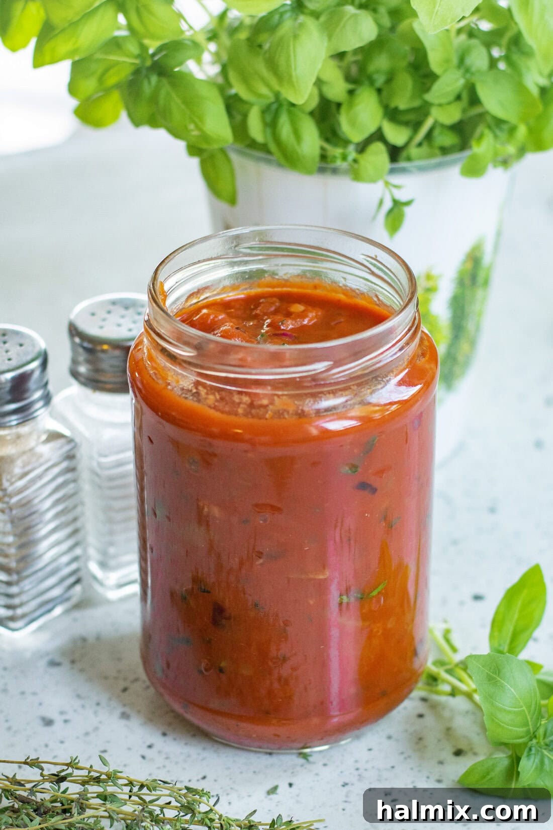 Classic Marinara Sauce 3 A glass jar filled with vibrant homemade marinara sauce, surrounded by fresh sprigs of basil and oregano.
