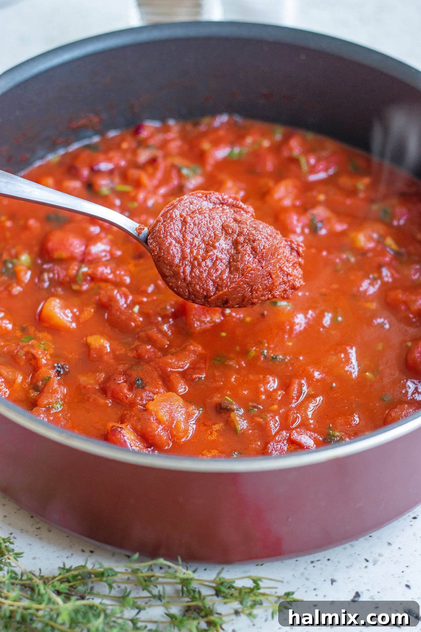 A spoon adding a dollop of rich tomato paste into a pot filled with aromatic ingredients for marinara sauce.