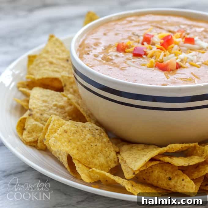 Warm, melty chili cheese dip in a white bowl, ready to be scooped with a chip.