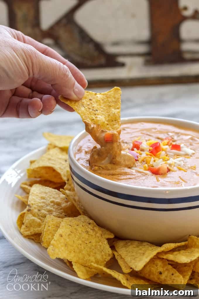 A close-up of the bubbling hot chili cheese dip in a serving bowl, garnished with a few tortilla chips.