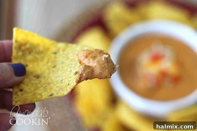 A close-up of a serving of chili cheese dip on a tortilla chip, highlighting the texture and melted cheese.