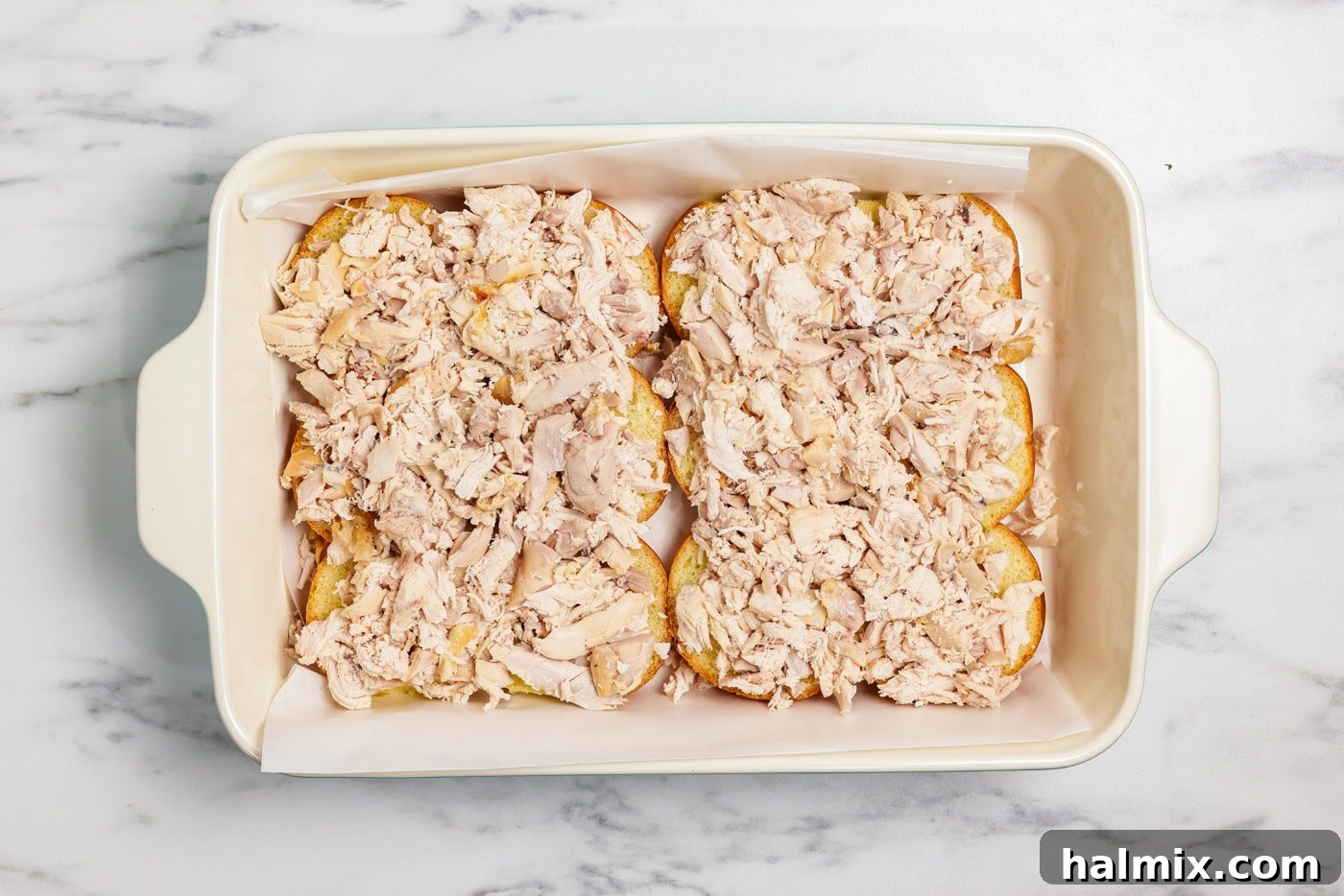 Shredded chicken generously layered on slider buns in a baking dish