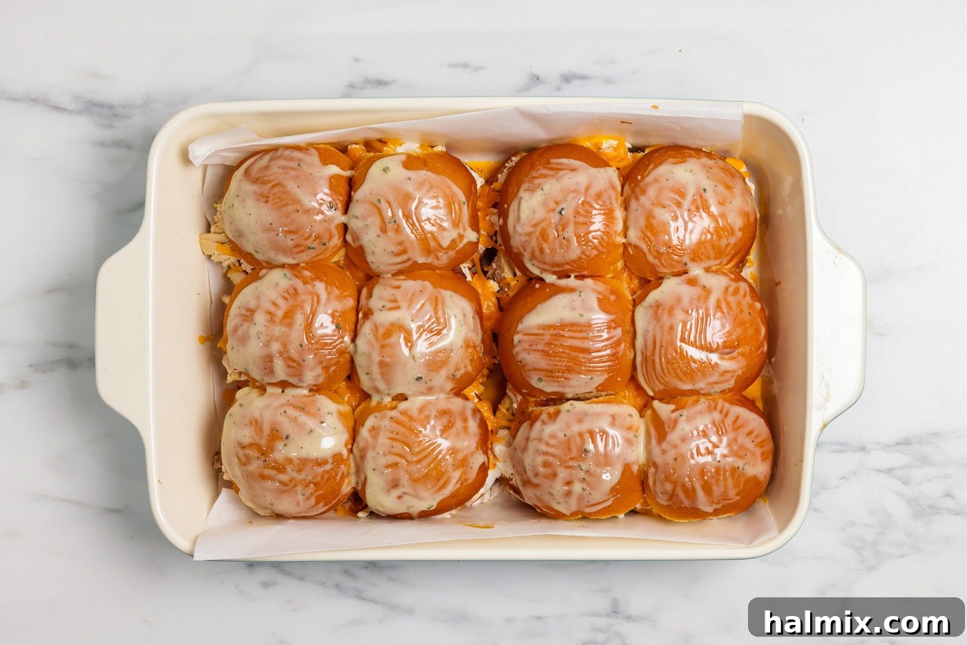 Melted butter and ranch seasoning mix basted over chicken bacon ranch sliders in a baking dish