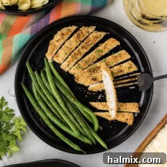 Plate of Parmesan Crusted Chicken cut into slices with green beans on the side