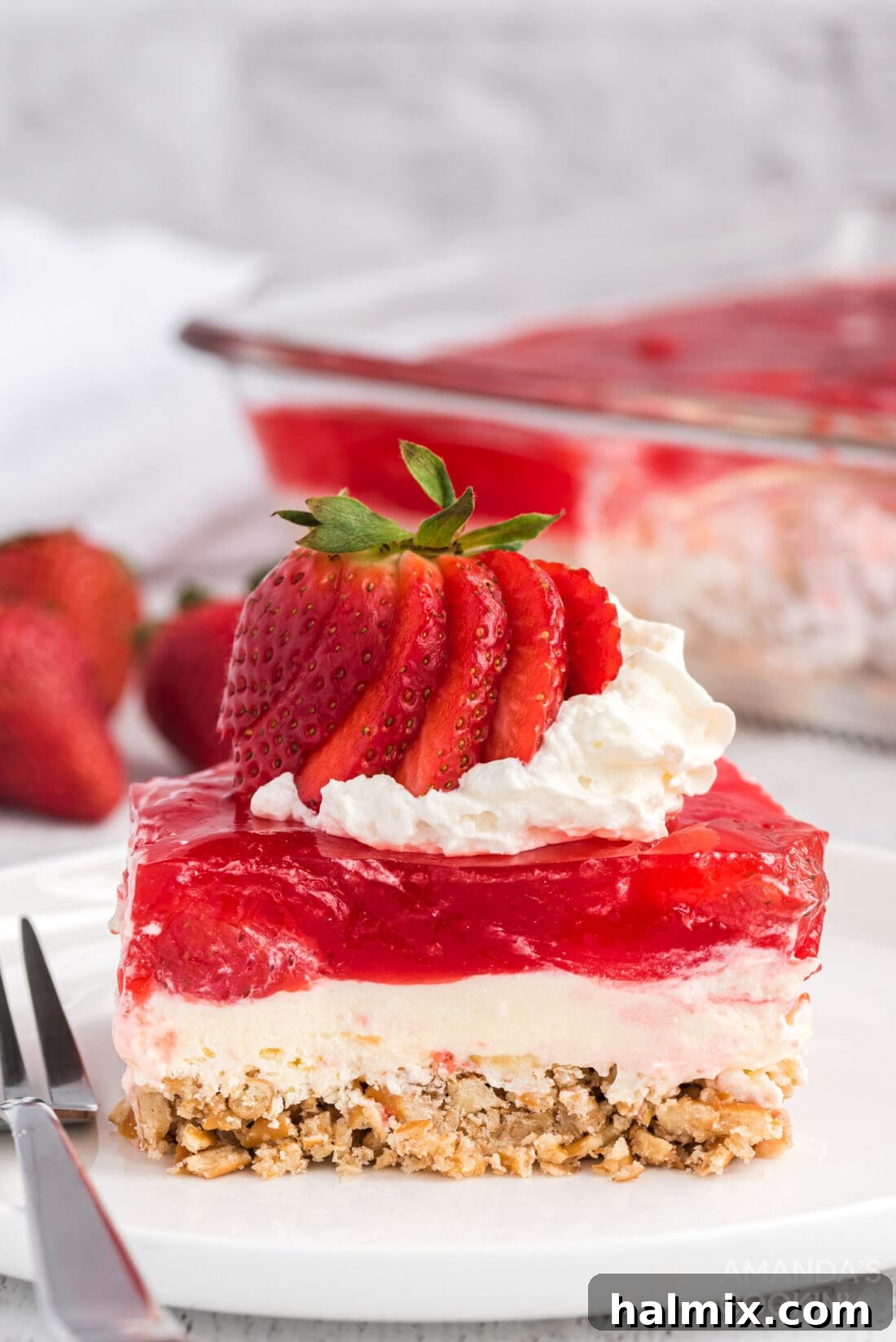 A vibrant slice of Strawberry Pretzel Salad, showcasing its distinct layers of pretzel crust, creamy white filling, and strawberry jello with fruit.
