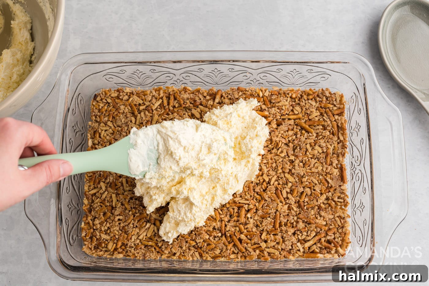 Spreading the smooth cream cheese layer over the cooled pretzel crust, forming an even, solid layer.
