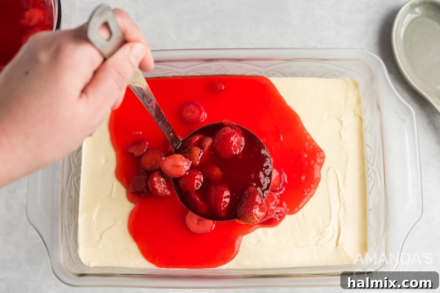 Gently pouring the partially set strawberry gelatin over the cream cheese layer in the baking dish, creating the final top layer.