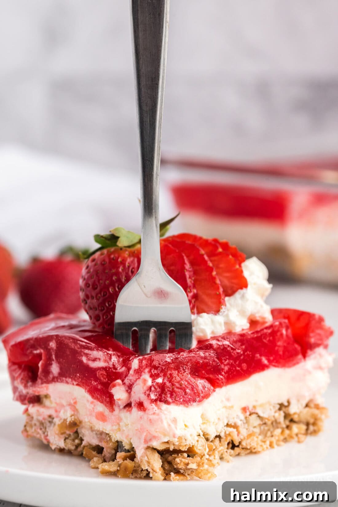 A fork is gently pressed into a slice of Strawberry Pretzel Salad, highlighting its inviting texture and layers.