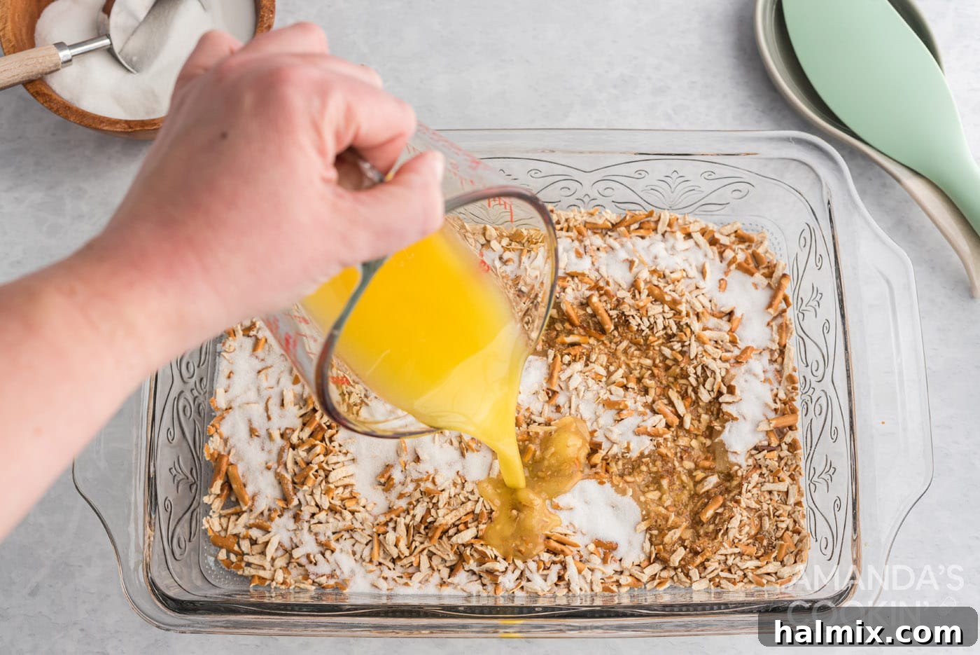 Adding melted butter to crushed pretzels and sugar in a baking pan, preparing the crust.