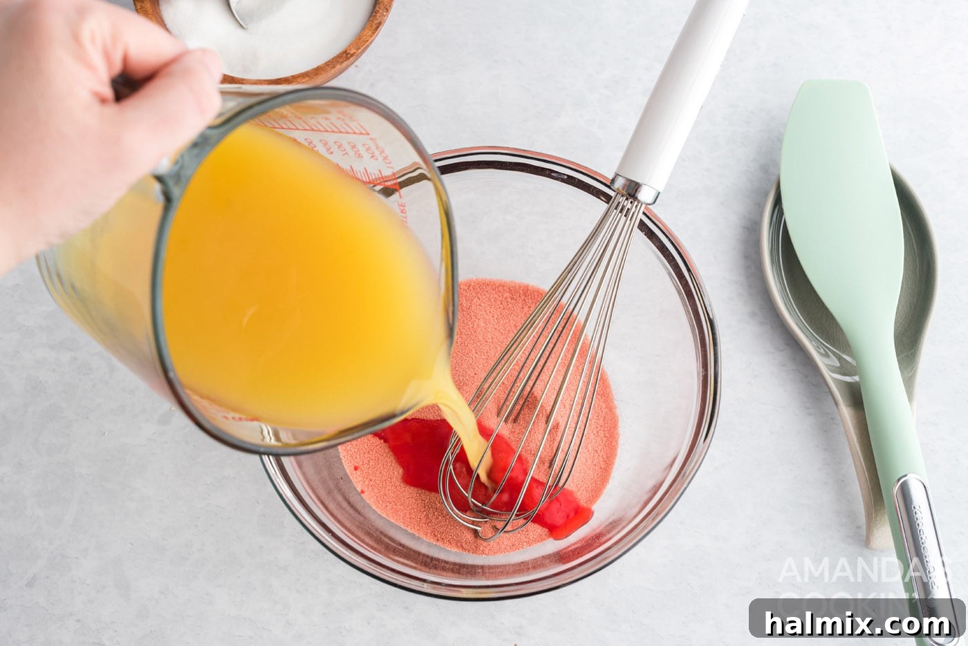 Pouring hot pineapple juice into strawberry gelatin powder in a bowl, a key step for enhanced flavor.