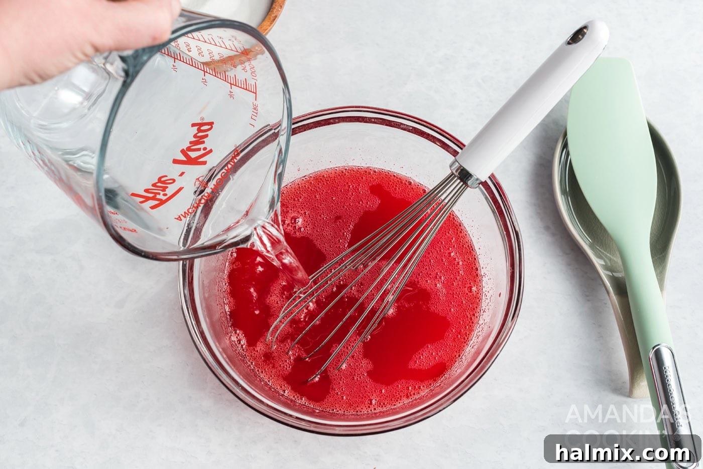 Adding cold water to the dissolved strawberry jello mixture, completing the liquid base.