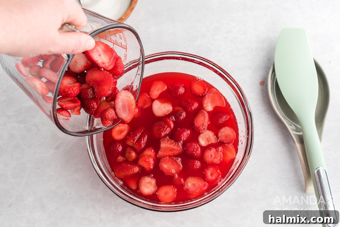 Adding sliced fresh strawberries into the partially set gelatin mixture, ensuring even fruit distribution.