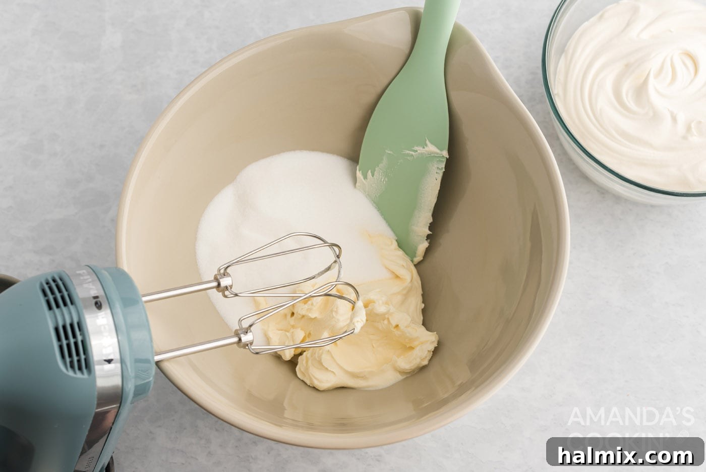 Cream cheese and sugar being beaten together in a mixing bowl with an electric mixer, creating a smooth base.