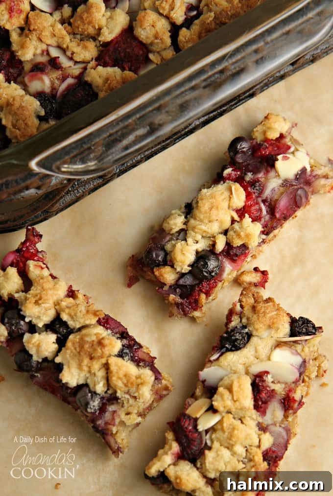 A close up overhead photo of three golden-brown berrylicious cookie bars, showcasing the mixed berry topping and crumbly texture.