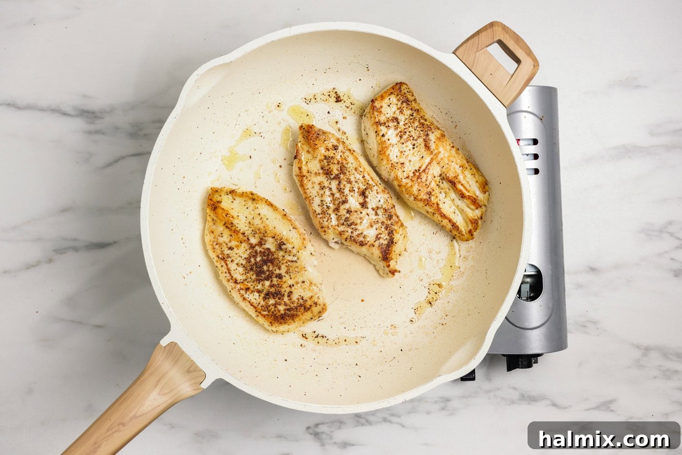 Chicken breasts cooked to a golden brown in a skillet with olive oil.