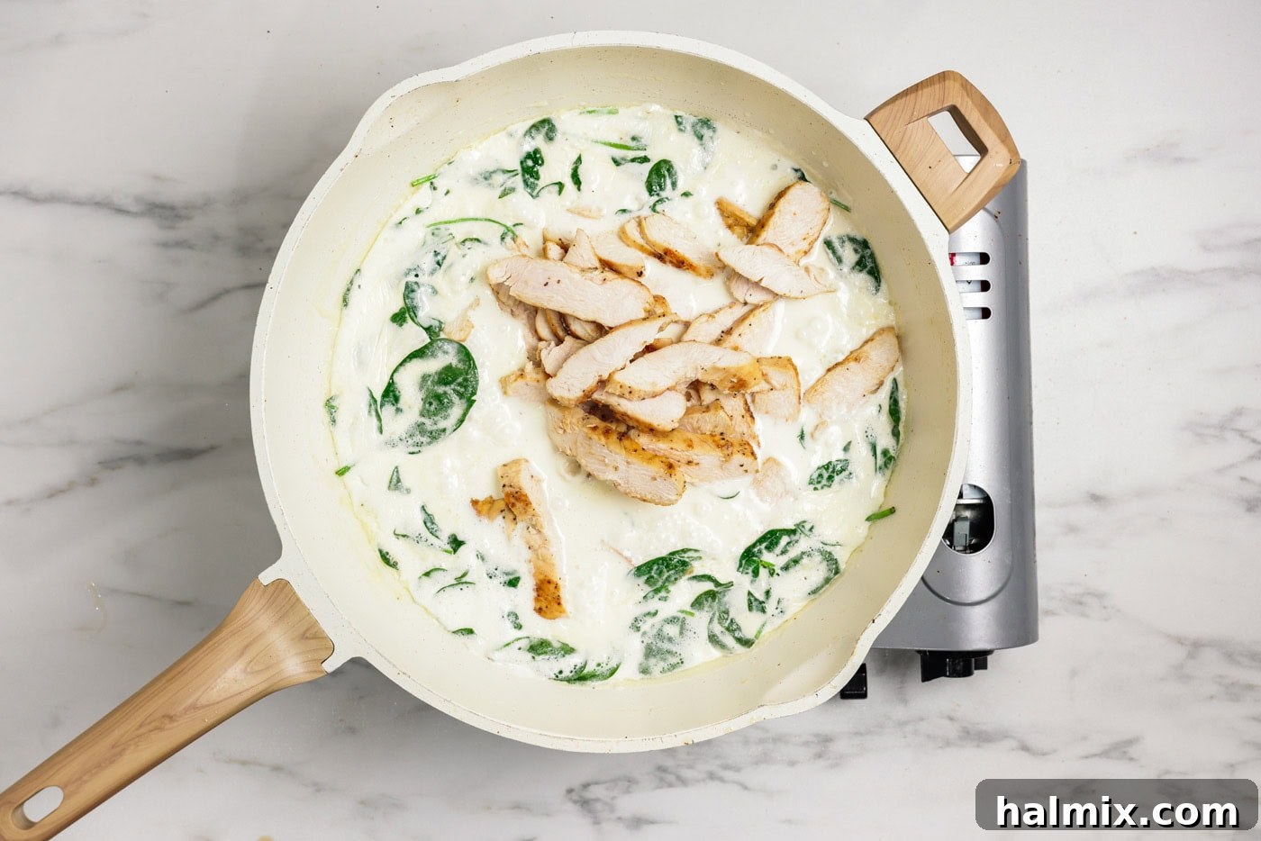 Spinach and sliced chicken being added to the garlic cream sauce in a skillet.
