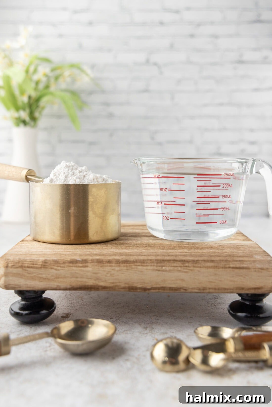 A dry measuring cup filled with flour sits beside a glass liquid measuring cup filled with water, illustrating the difference between measuring dry and liquid ingredients.