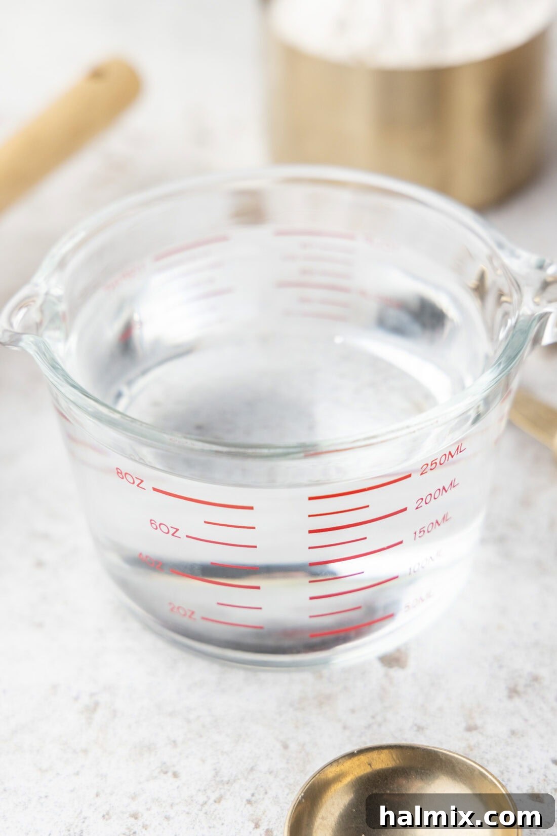 A transparent glass measuring cup filled with water, clearly showing the measurement markings for cups, fluid ounces, and milliliters.