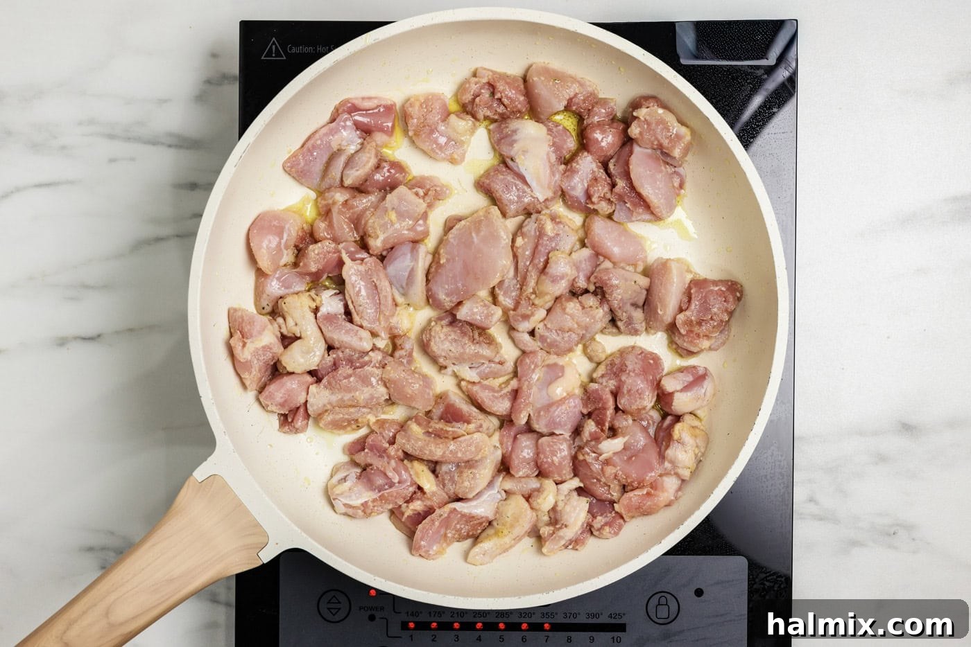 Cubes of chicken coated in flour cooking in a skillet with oil