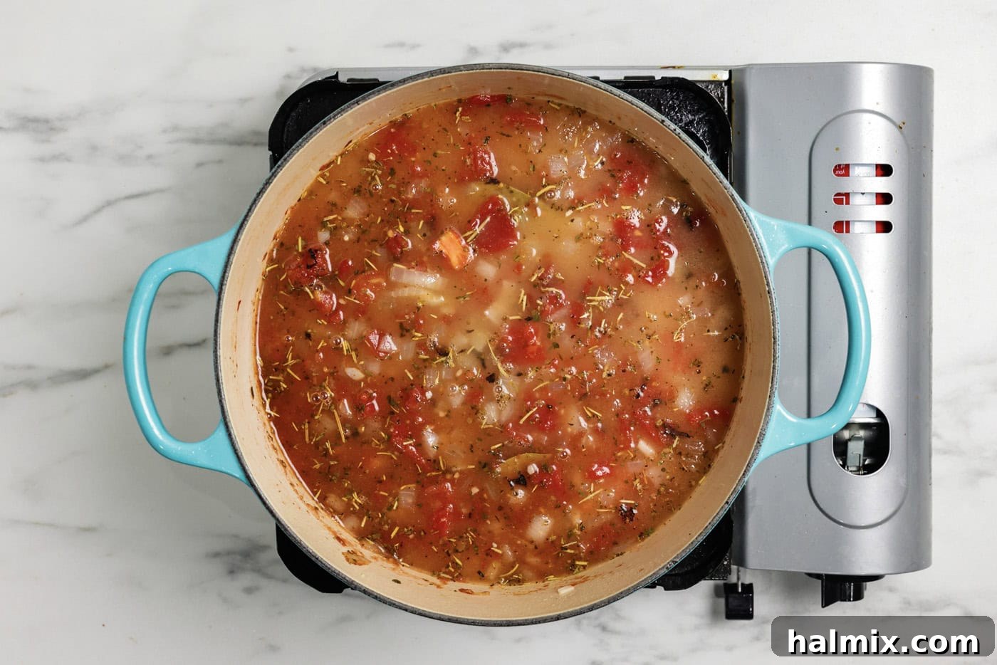 Chicken broth added to pot with aromatic tomato base, simmering to perfection.