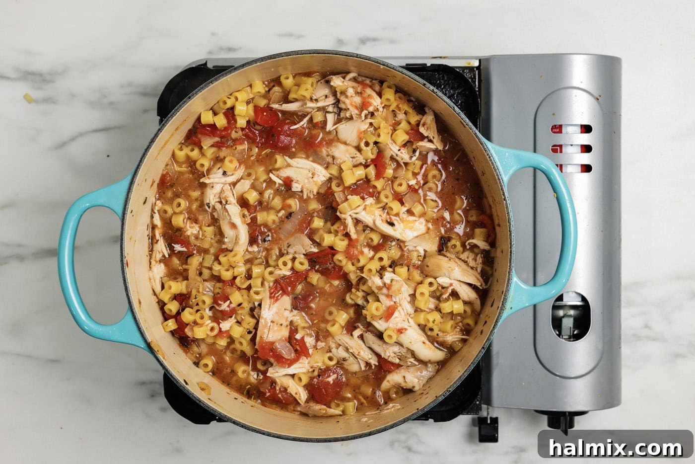 Ditalini pasta and shredded chicken added to the pot of chicken parmesan soup, creating a hearty meal.