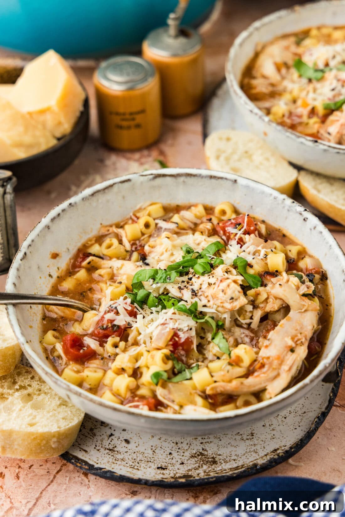 Close up photo of a bowl of Chicken Parmesan Soup topped with fresh parmesan and basil, ready to eat.