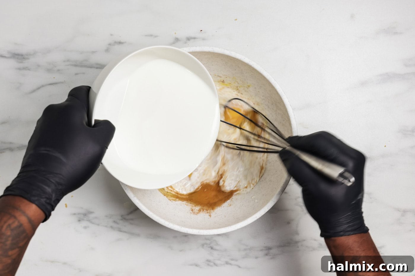 Baked French Toast Delight 5 Hand pouring whole milk into bowl while whisking