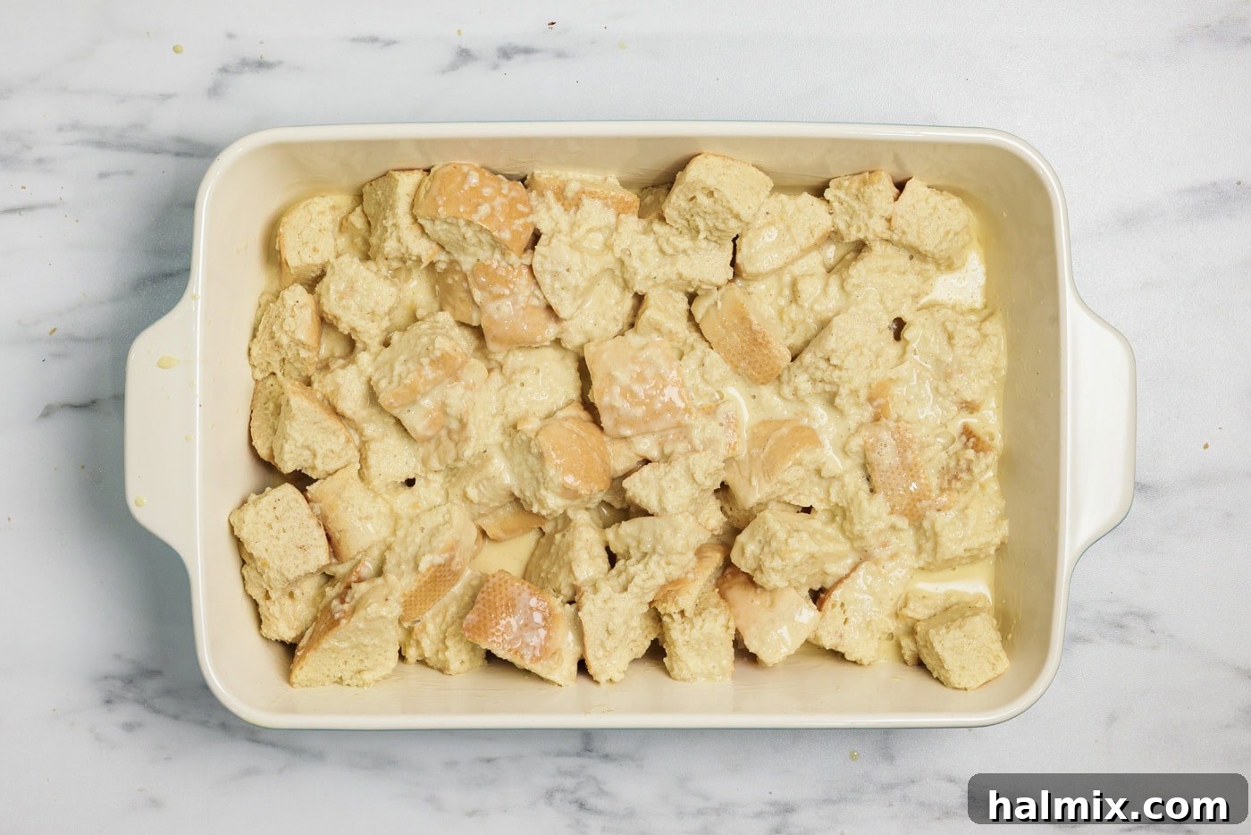 Soaked bread cubed in a baking dish, covered with plastic wrap