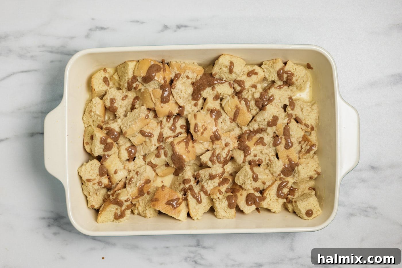 Cinnamon butter mixture drizzled over French toast casserole in a dish before baking