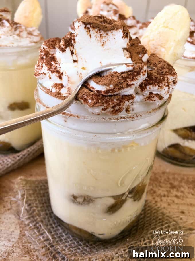 A close-up photo of a tiramisu trifle in a mason jar with a spoon, ready to be enjoyed.