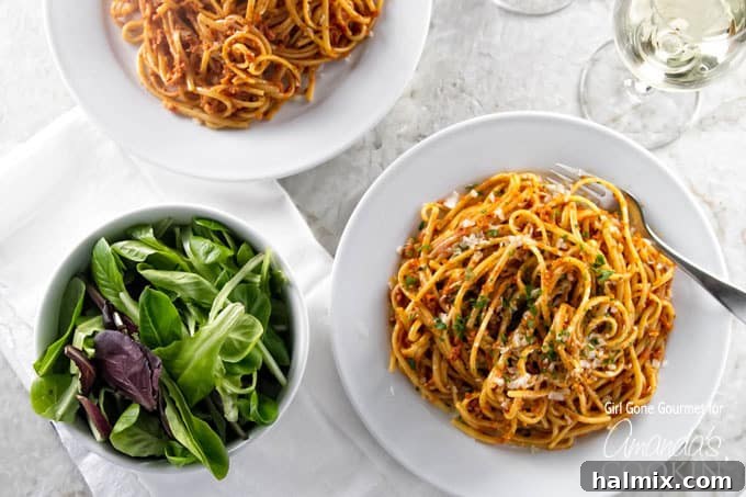 Mediterranean Sun-Kissed Pesto 4 An overhead photo of two plated of sun dried tomato pesto on pasta with a salad on the side, ready to be served.