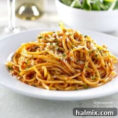 A photo of sun dried tomato pesto on pasta on a white plate, garnished with fresh herbs.