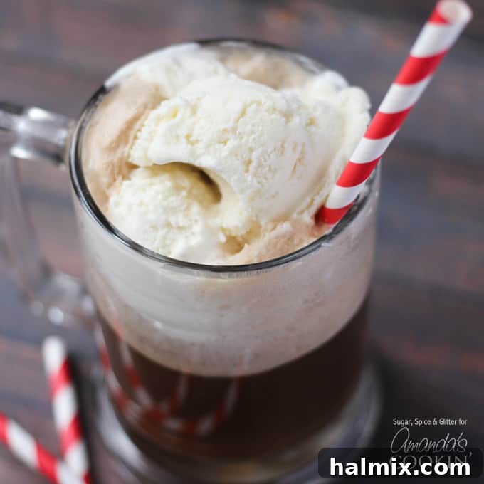 A close-up photo of a root beer float cocktail in a clear mug served with a red and white striped straw, emphasizing its delightful froth.