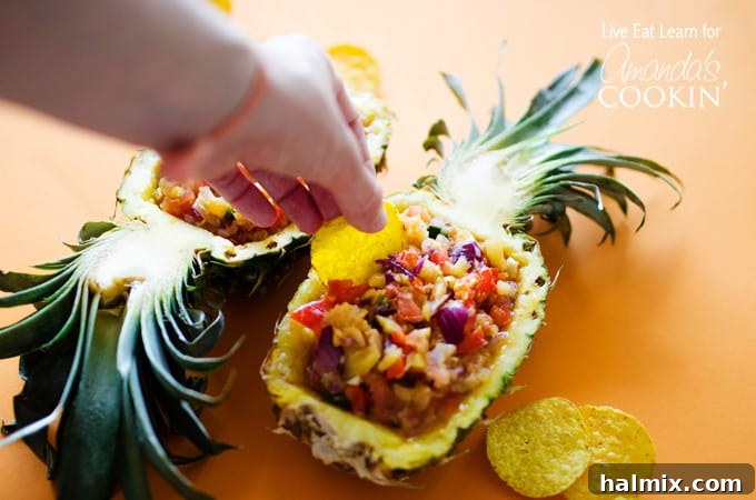 A photo of a tortilla chip scooping pineapple salsa from a halved pineapple, showcasing the perfect texture.