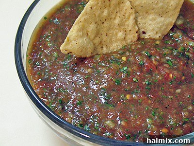 A close up photo of pineapple salsa in a clear bowl with two tortilla chips dipped in, showing a chunky texture.