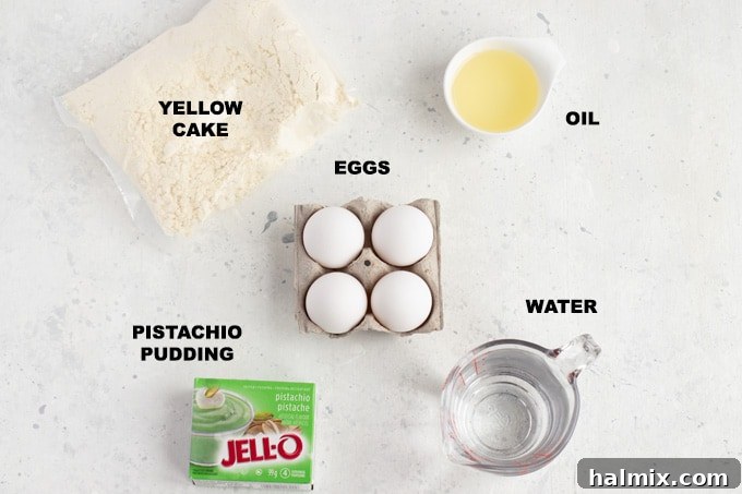 All the essential ingredients for making the pistachio cake laid out on a kitchen counter, including a yellow cake mix box, pistachio pudding mix, eggs, vegetable oil, and water.