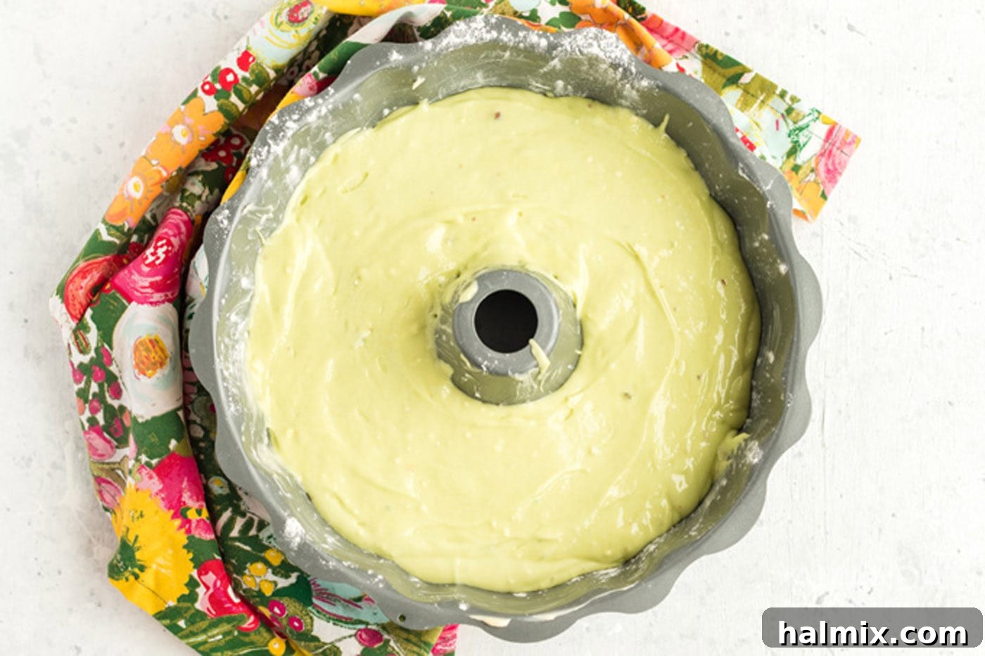Smooth, pale green pistachio cake batter being poured into a greased bundt pan, ready for baking.
