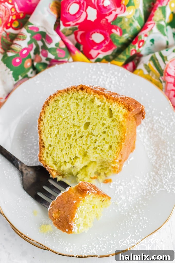 A tempting slice of moist pistachio cake, garnished with a light dusting of powdered sugar, presented on a dessert plate, showcasing its tender texture.