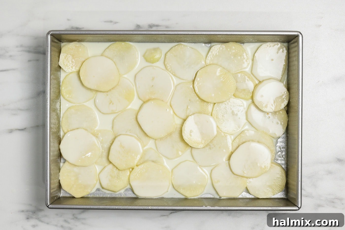Broth sauce mixture on top of sliced potato rounds in a baking pan