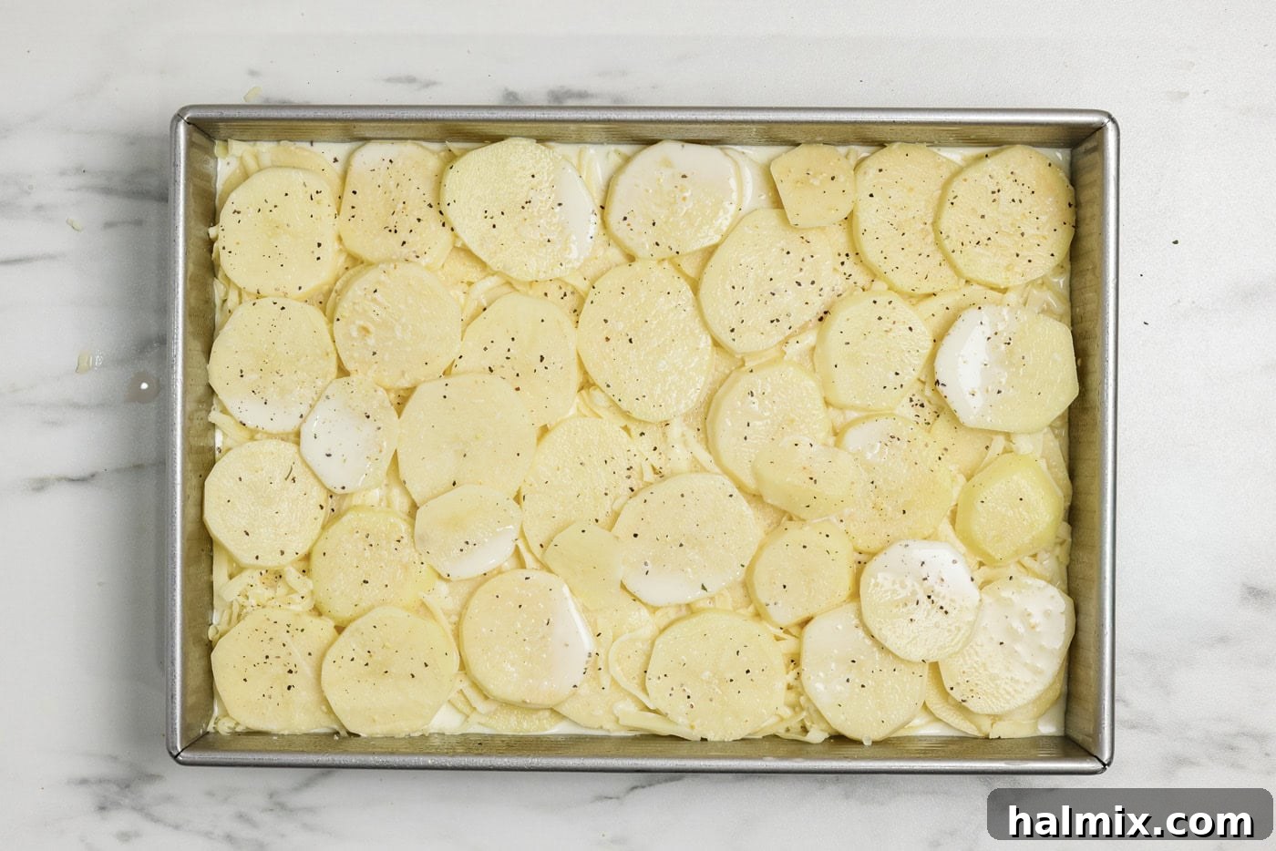 sliced potato layer on top of cream sauce and cheese in a baking pan