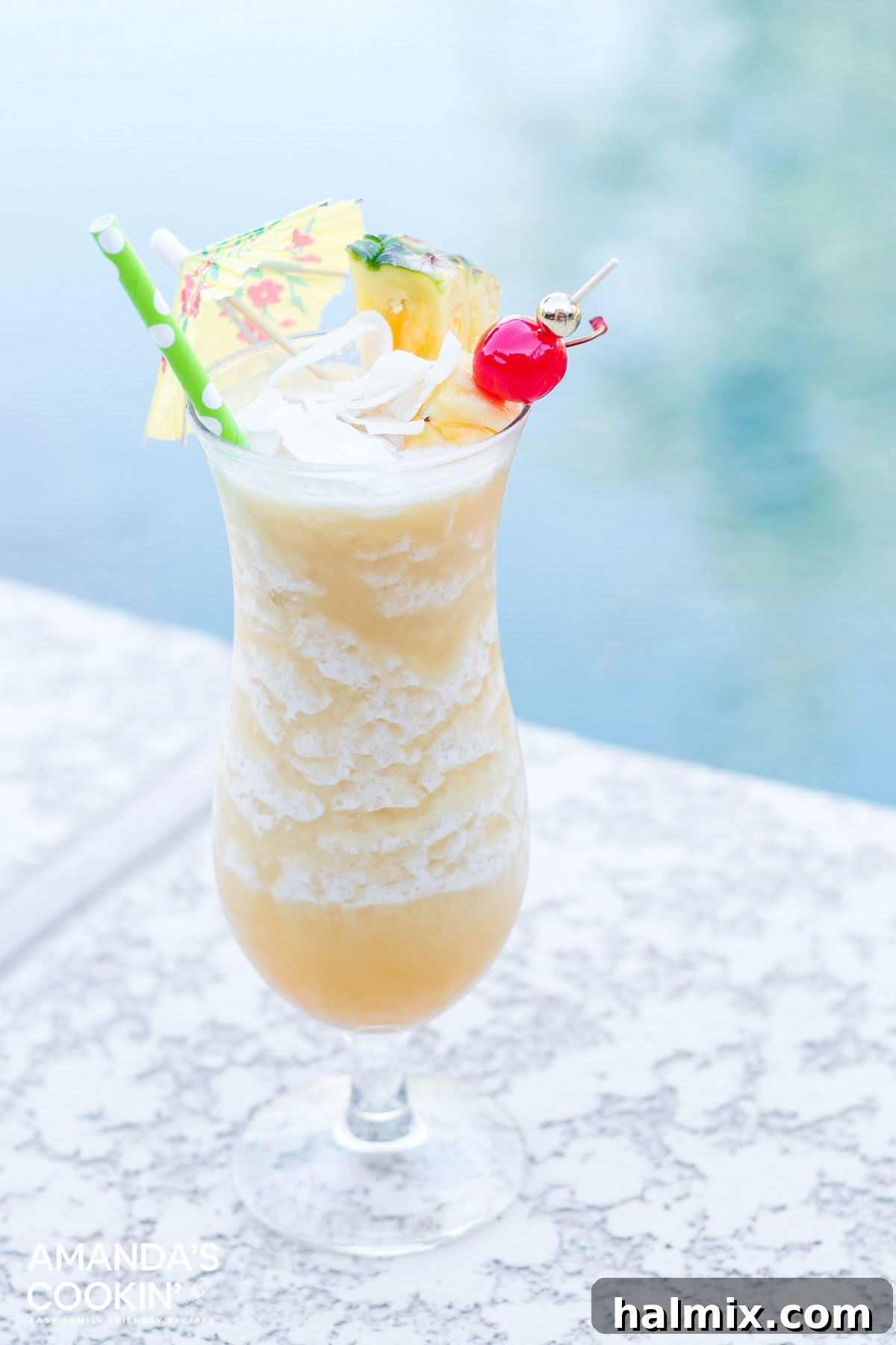 A perfectly frosted Pina Colada, garnished with a pineapple wedge and cherry, sits invitingly by a swimming pool on a sunny day.